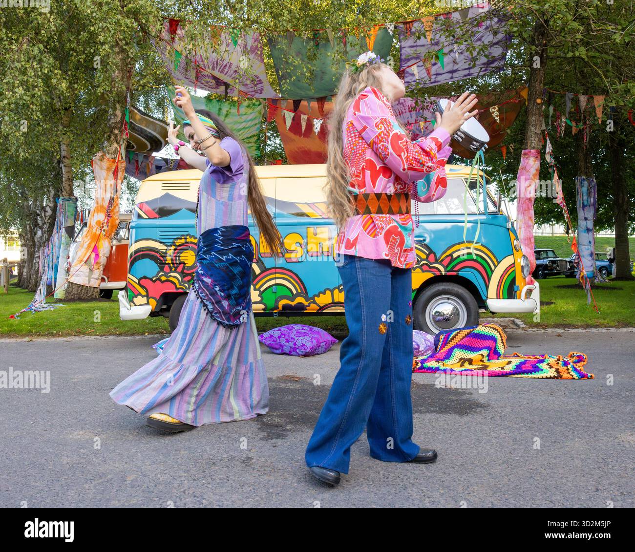 Ricreazione dell'era hippy della fine degli anni '60 con due donne danzanti e camper psichedelico Volkswagen sullo sfondo. Goodwood Revival, Sussex, Regno Unito Foto Stock