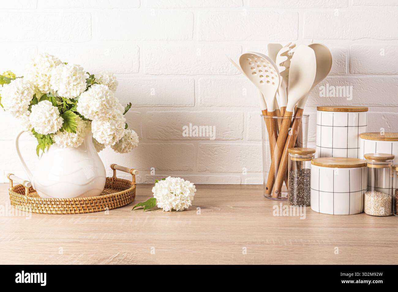 Un set di strumenti per cucinare gli alimenti in un supporto, un set di vasi in ceramica bianca, una caraffa con rami fioriti in un piano di legno. Stile ecologico Foto Stock