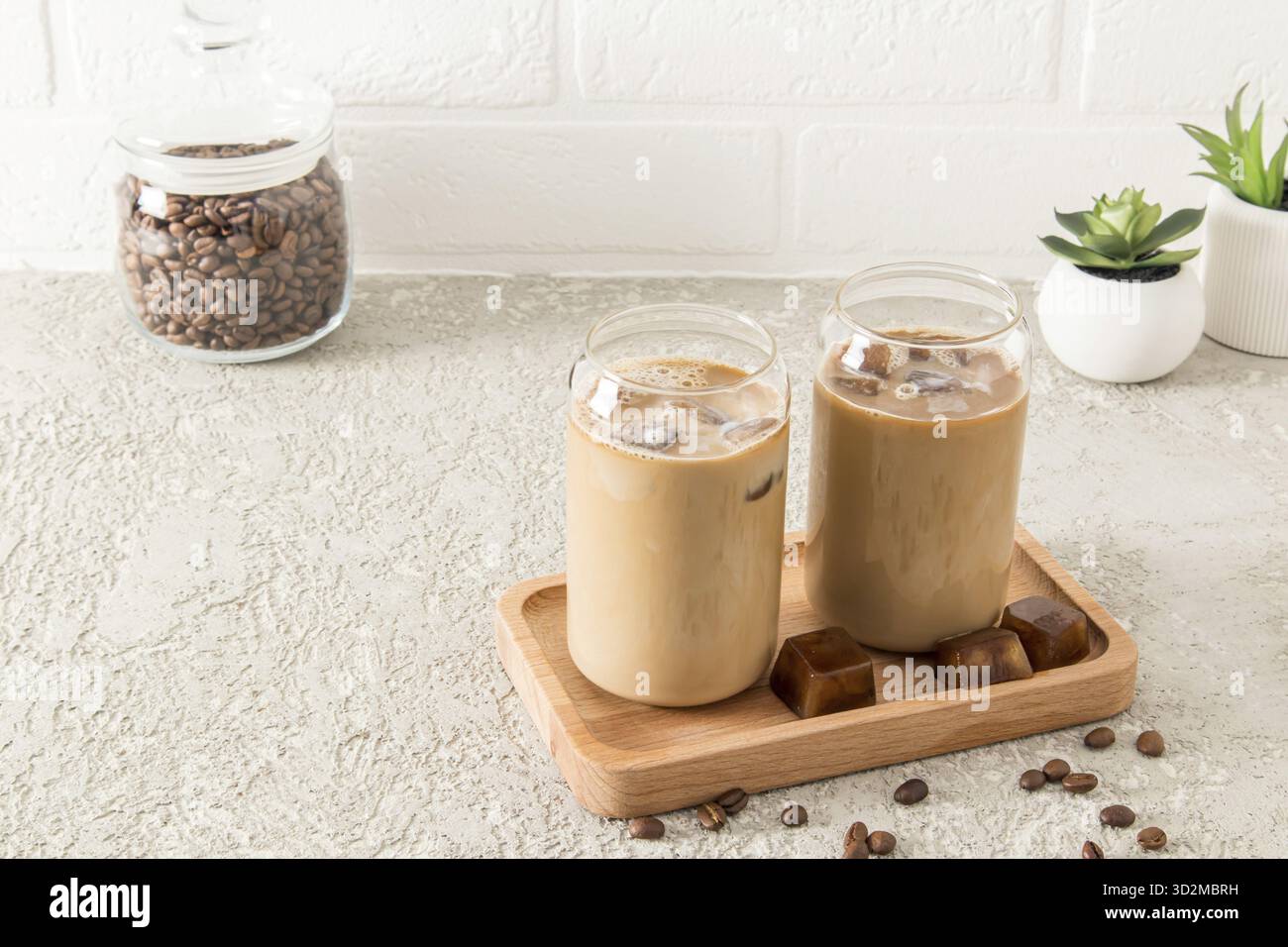 Due bicchieri moderni a forma di barattolo di caffè freddo, una bevanda al cioccolato o moka su un vassoio di legno di fronte a una parete di mattoni bianchi Foto Stock