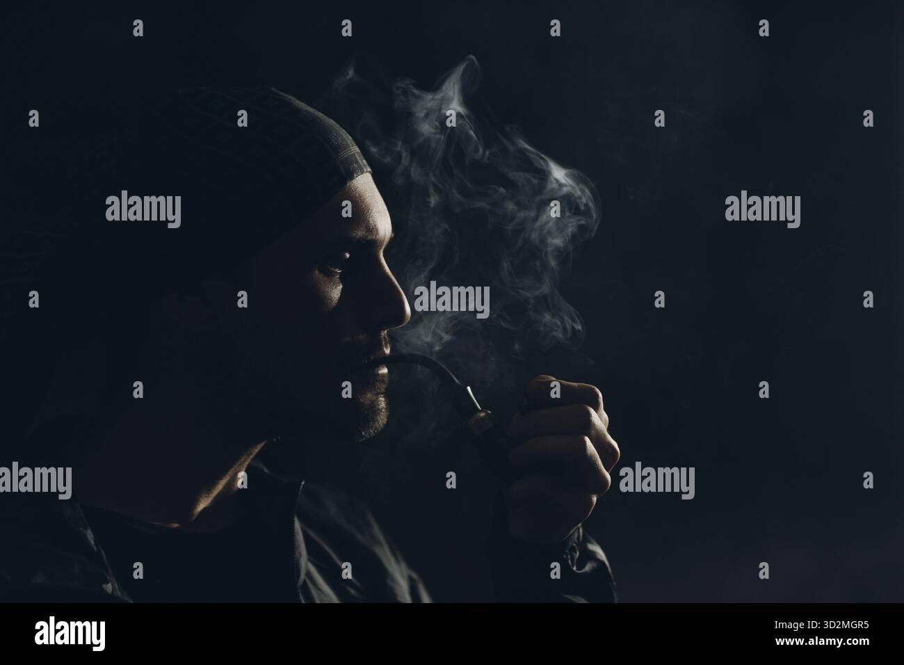 L'uomo fuma il tubo di fumo su sfondo scuro. Lato posteriore illuminato profilo verticale con fumo Foto Stock