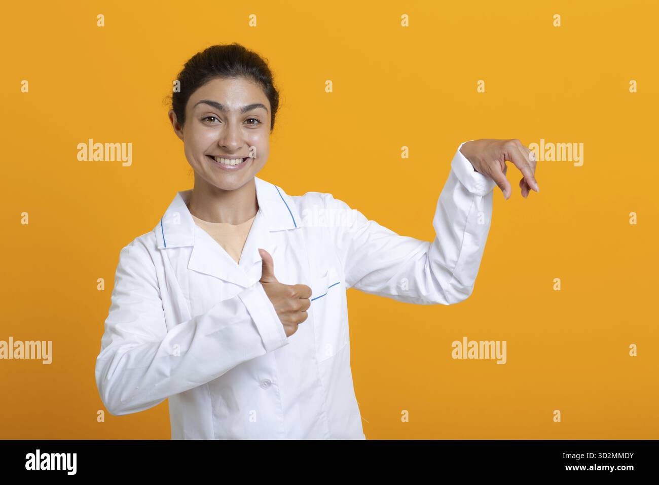 Ritratto della donna medica indiana in abito medico bianco che tiene le dita modello vaccino covid-19 o altre cose mediche isolate su sfondo giallo Foto Stock