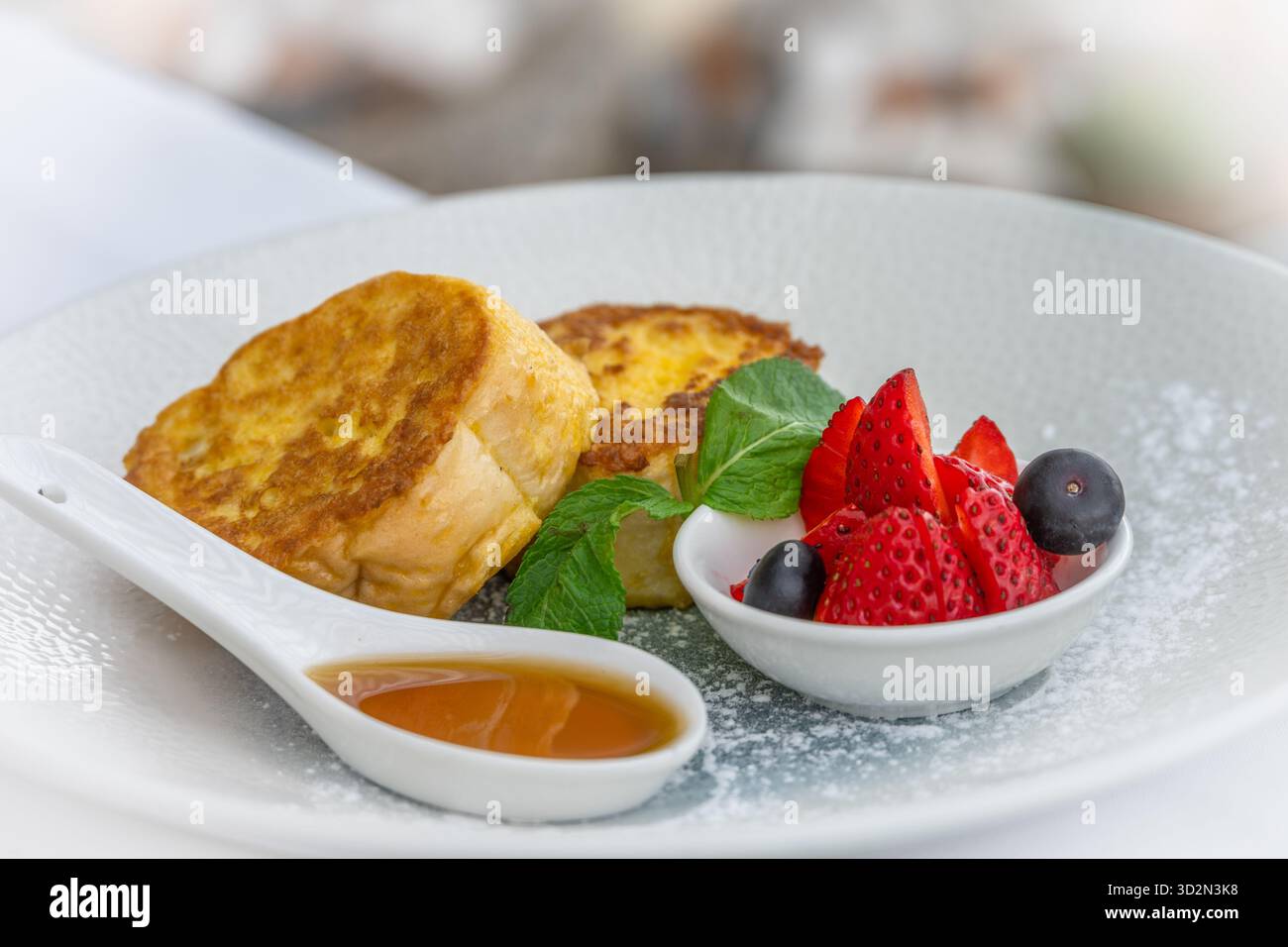 Toast alla francese con sciroppo e frutti di bosco su un piatto bianco, colazione calda Foto Stock