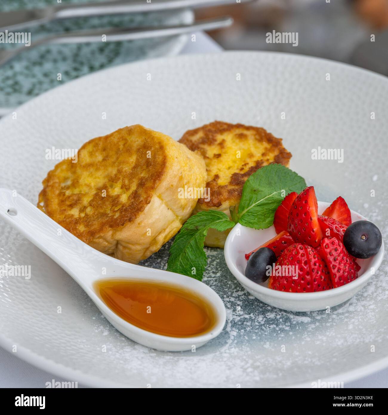 Toast alla francese con sciroppo e frutti di bosco su un piatto bianco, colazione calda Foto Stock