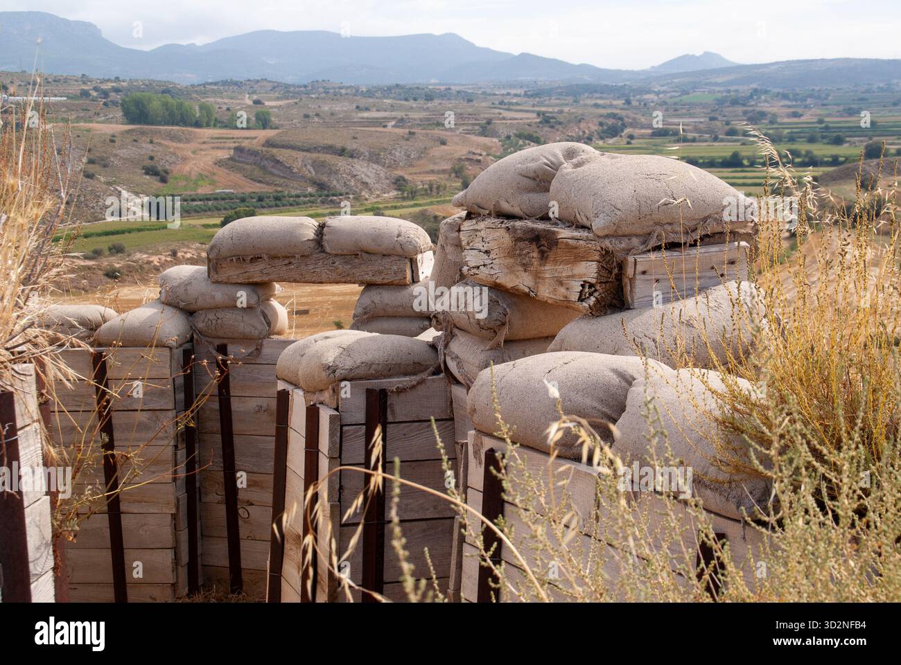 Trincea ricostruita in tempo di guerra con rinforzi in legno e sacchi di sabbia, che si affaccia su una valle con colline lontane Foto Stock