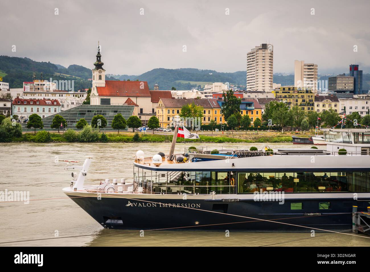 Linz, Austria - 2 luglio 2019: Avalon Waterways Impressions nave da crociera fluviale europea sul Danubio con la città vecchia e gli alti edifici sullo sfondo. Foto Stock