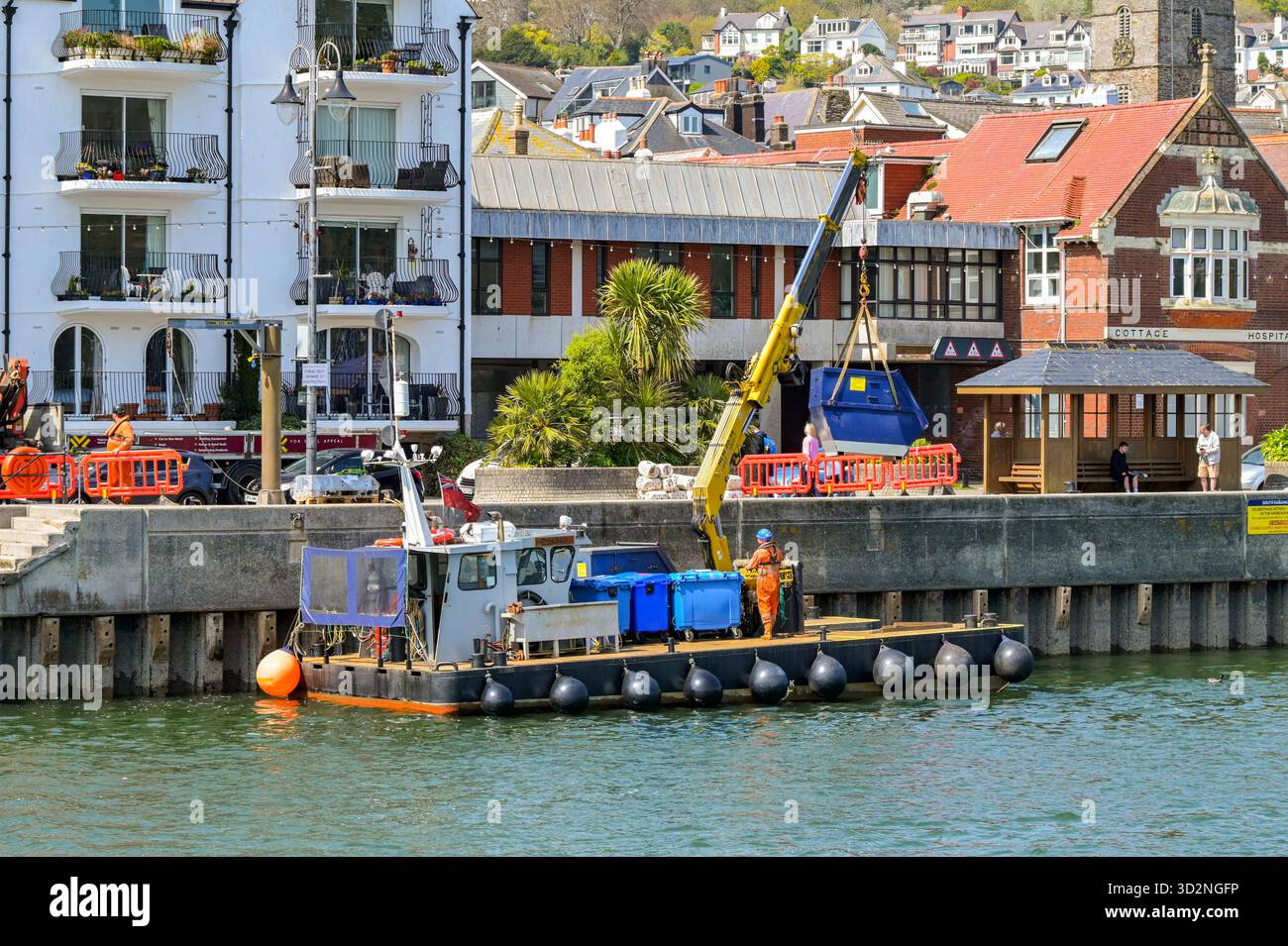 Dartmouth, Devon, Inghilterra, Regno Unito - 24 aprile 2025: Piccola imbarcazione industriale con gru idraulica sul ponte che carica un container sul ponte sul fiume Foto Stock