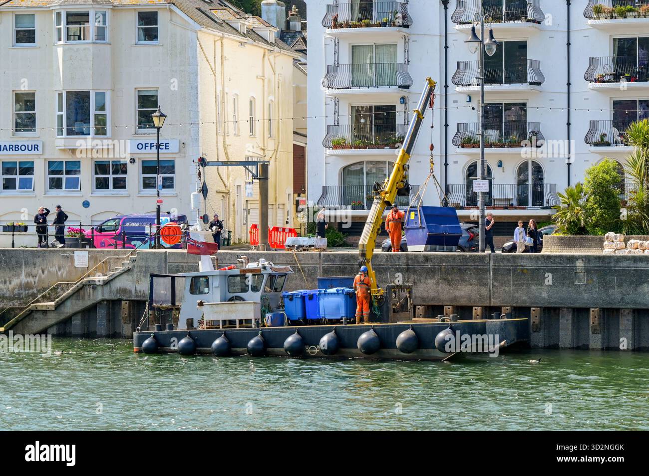 Dartmouth, Devon, Inghilterra, Regno Unito - 24 aprile 2025: Piccola imbarcazione industriale con gru idraulica sul ponte che carica un container sul ponte sul fiume Foto Stock