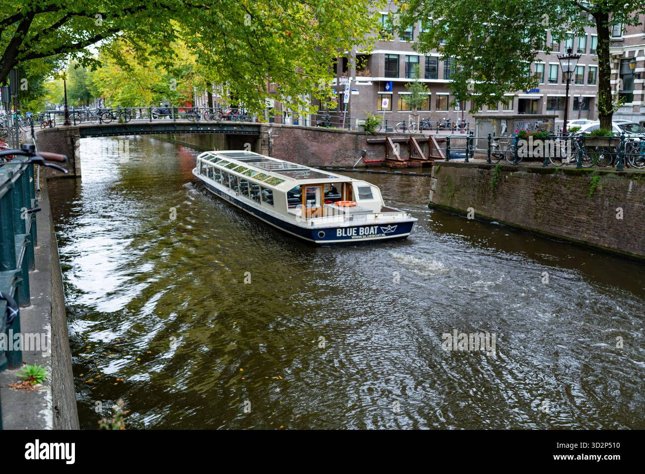 Tour in barca attraverso il canale di Amsterdam sotto un ponte alberato Foto Stock