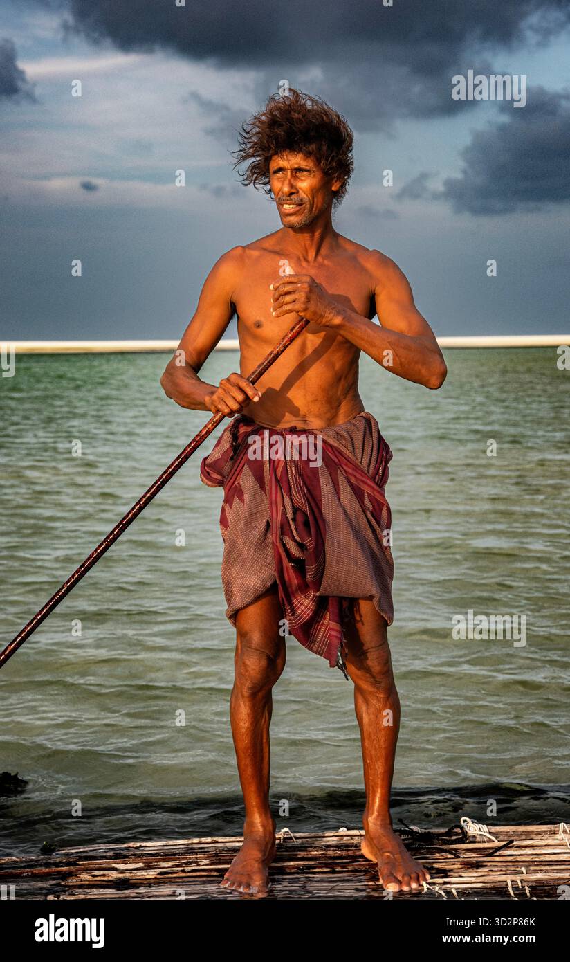 Un uomo di caverna si erge orgogliosamente su una zattera nella laguna di Detwah, Socotra, mostrando uno stile di vita unico su uno sfondo nuvoloso. Foto Stock