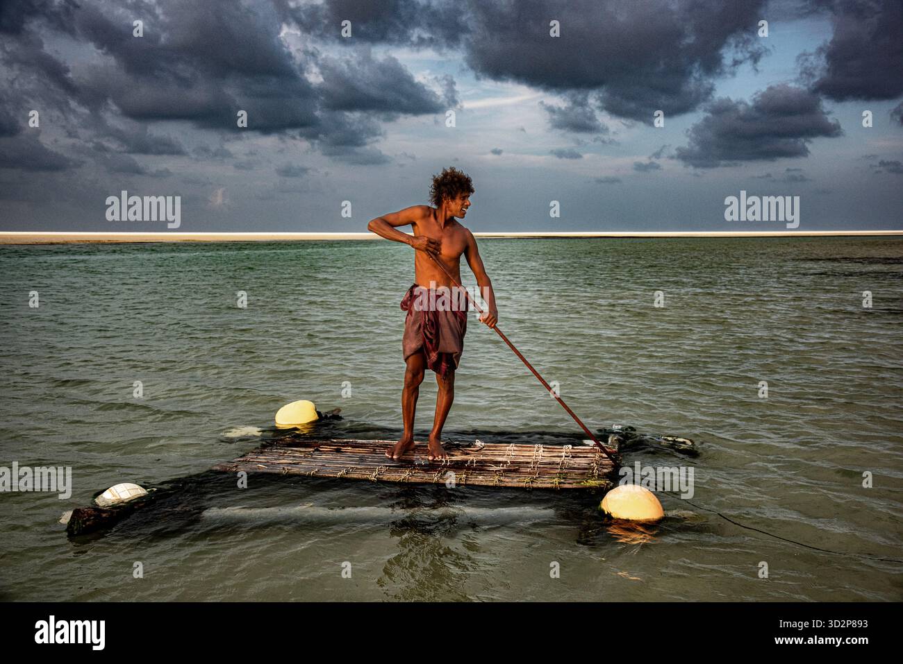 Un uomo di caverna si erge orgogliosamente su una zattera nella laguna di Detwah, Socotra, mostrando uno stile di vita unico su uno sfondo nuvoloso. Foto Stock