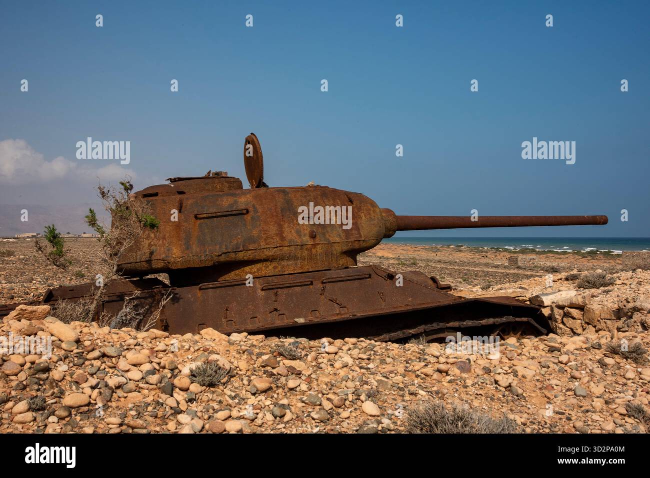 Un carro arrugginito sovietico giace parzialmente sepolto nella sabbia di Socotra, affacciato sulle splendide acque blu del Mar Arabico. Foto Stock