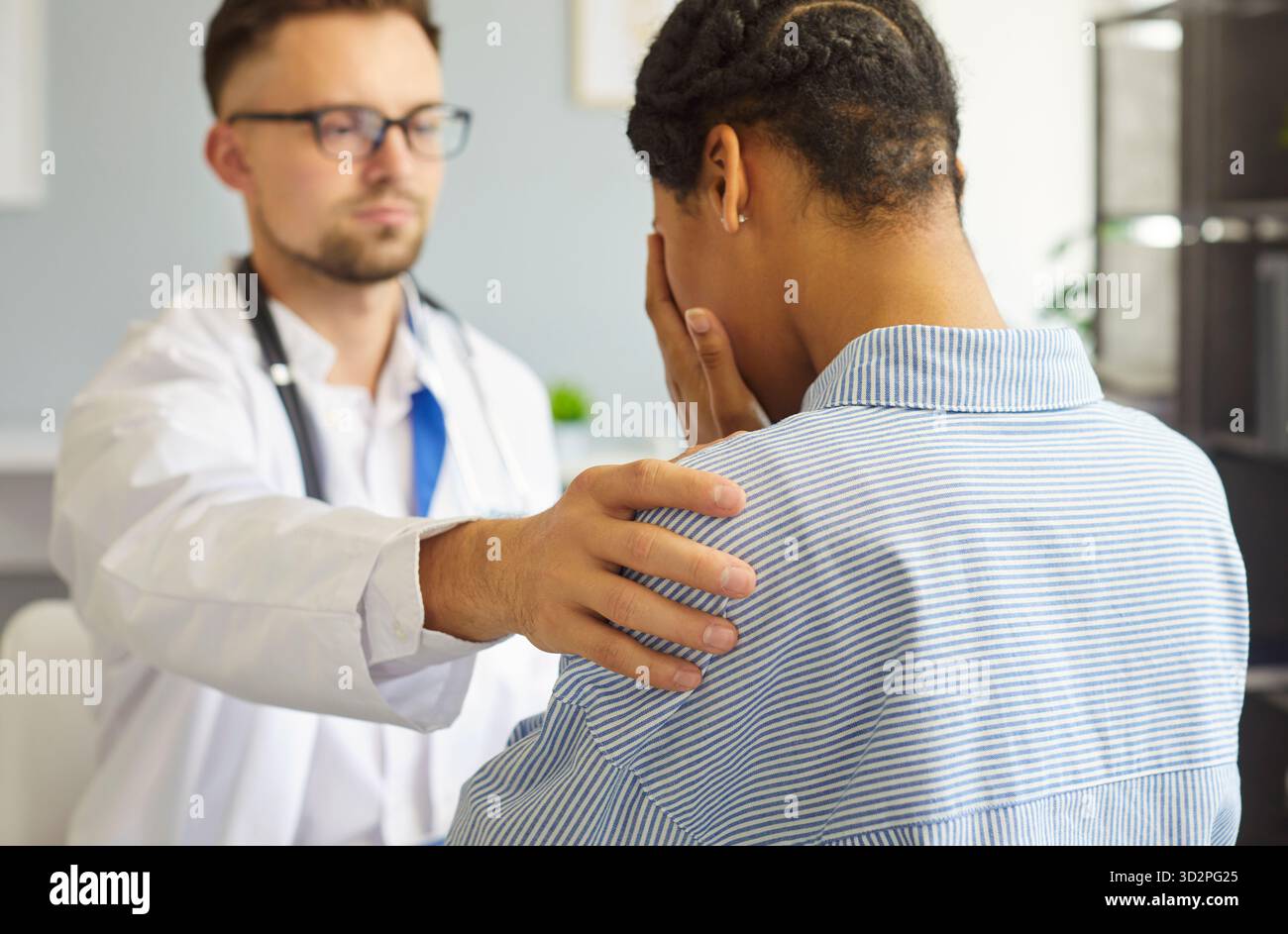 Giovane medico di sesso maschile sicuro di sé che sostiene paziente malato turbato donna che copre il viso con le mani in ufficio Foto Stock