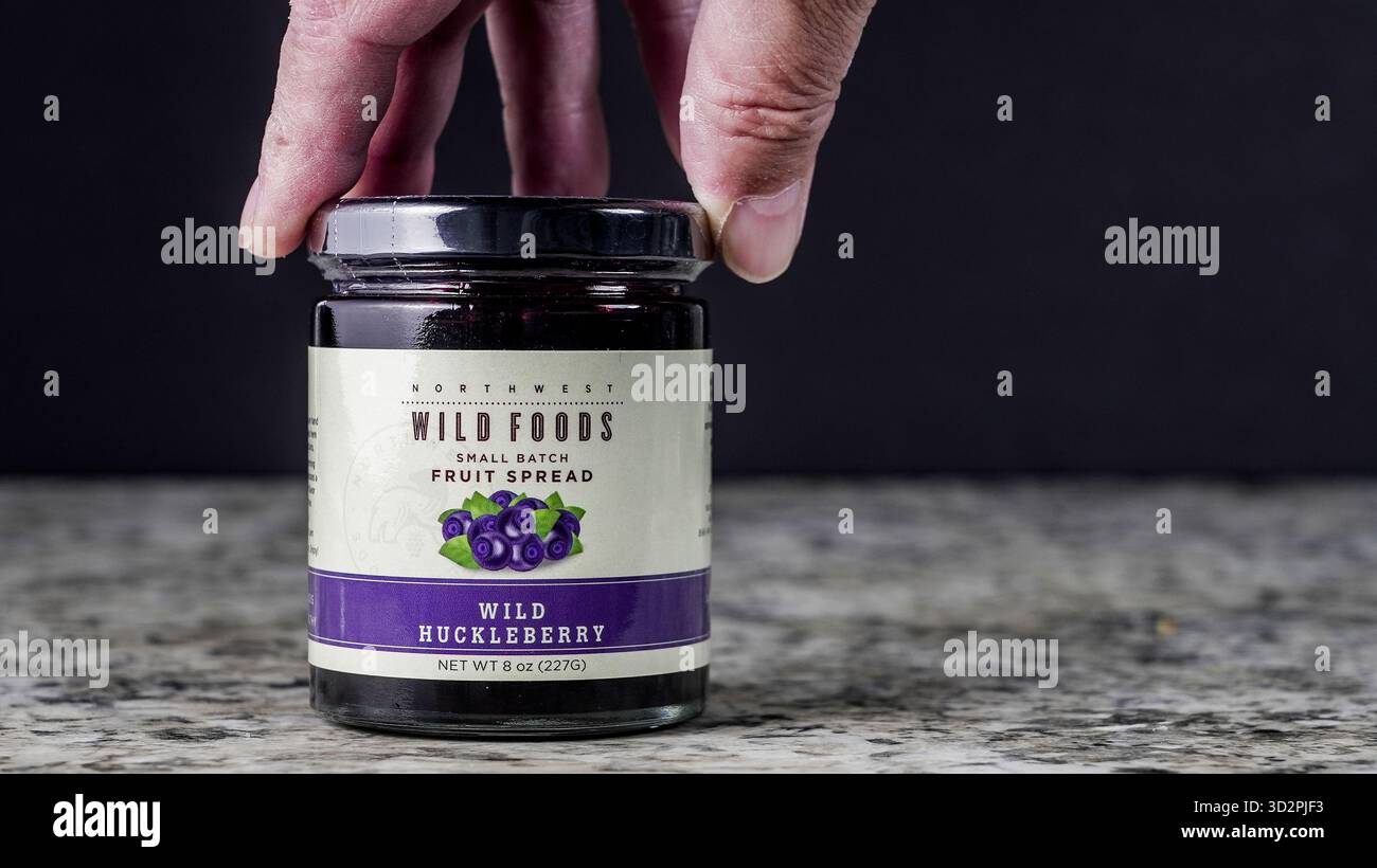 NORWALK, CT, Stati Uniti d'America - 30 OTTOBRE 2025: Una mano raggiunge un barattolo di frutta di ucoccola selvatica spalmata su un bancone della cucina. Il vaso è etichettato e visualizza i Foto Stock