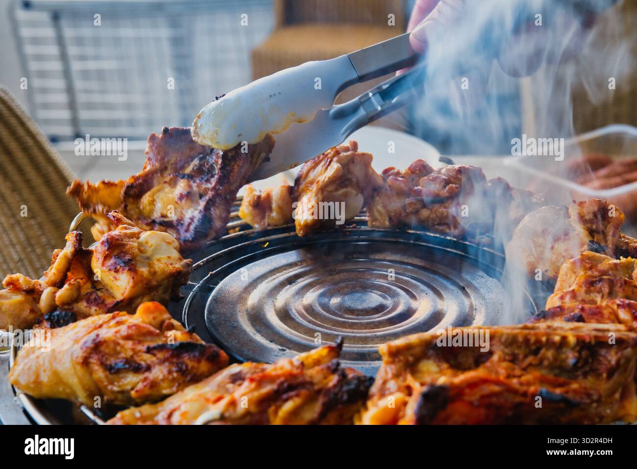 Barbecue di pollo grigliato affumicato all'aperto con pinze, carne arrosto succosa in cottura con affumicatura spessa durante il picnic estivo, preparazione barbecue sul cortile Foto Stock