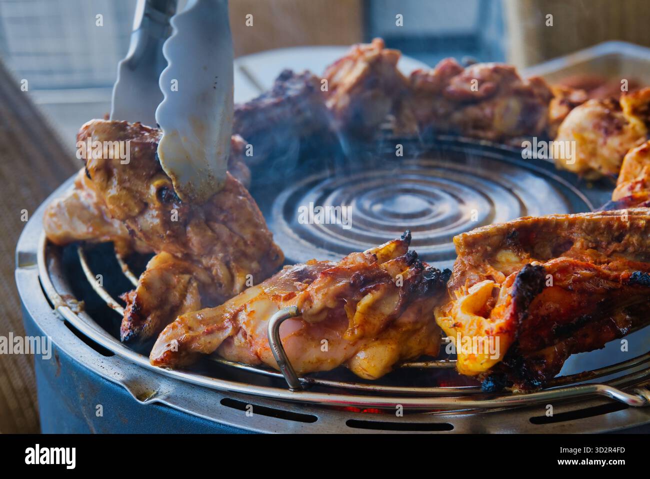 Barbecue di pollo grigliato affumicato all'aperto con pinze, carne arrosto succosa in cottura con affumicatura spessa durante il picnic estivo, preparazione barbecue sul cortile Foto Stock
