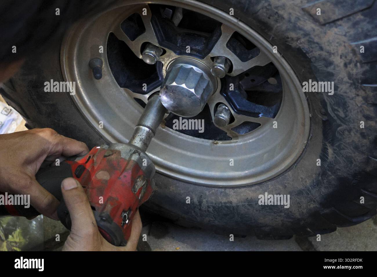 Meccanico specializzato che utilizza un attrezzo elettrico per la riparazione di ruote e pneumatici. Primo piano del servizio di manutenzione auto professionale in garage, mostrando i dettagli del cliente Foto Stock