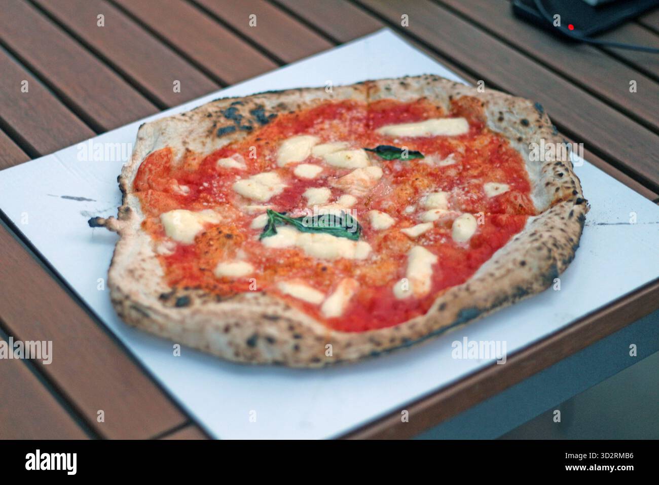 Primo piano di una tradizionale pizza margherita napoletana condita con salsa di pomodoro, mozzarella fusa e basilico fresco servito su un vassoio di carta Foto Stock