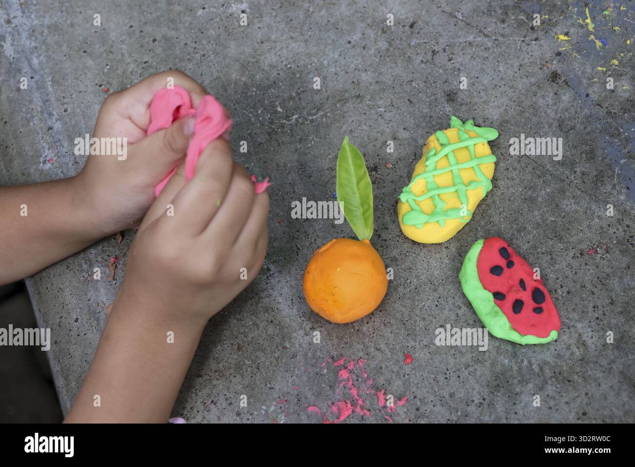 Le mani dei bambini modellano l'impasto colorato in forme di frutta come anguria, ananas e arancia, mostrando creatività e divertente attività di apprendimento Foto Stock