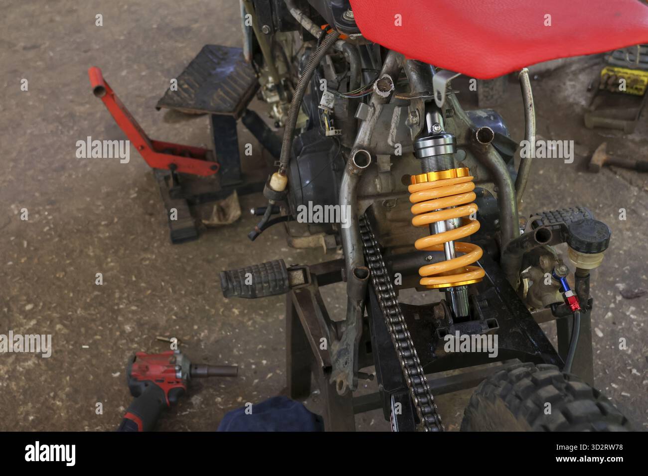La moto da neve è in fase di riparazione all'interno del garage. Primo piano sul progetto di restauro della motocicletta, con l'ammortizzatore giallo, il motore e la catena. Mecha dettagliato Foto Stock