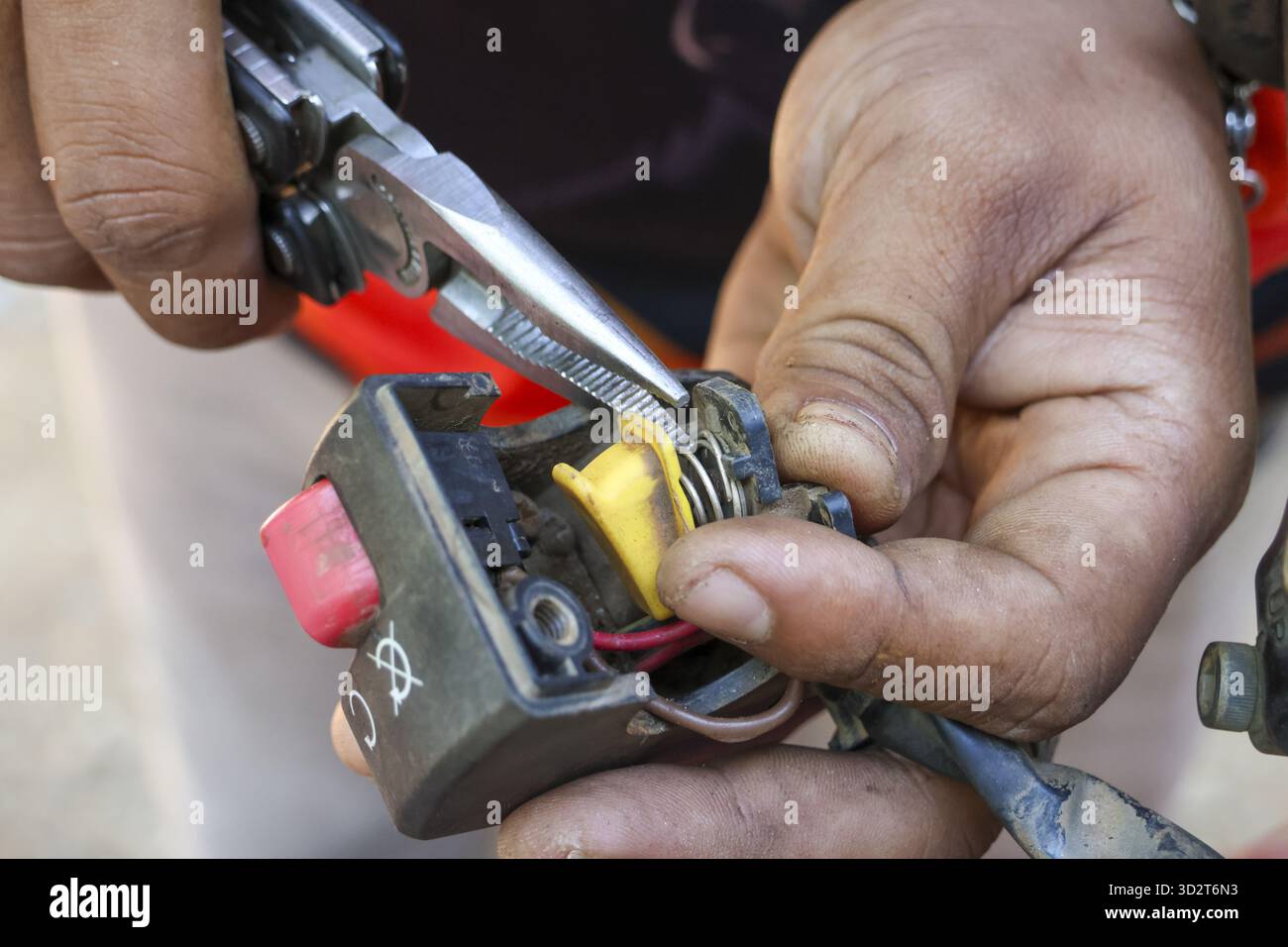 Primo piano del meccanico che esegue la riparazione sull'interruttore della motocicletta. tecnico qualificato che fissa un filo elettrico con pinze durante la messa a fuoco del veicolo principale Foto Stock