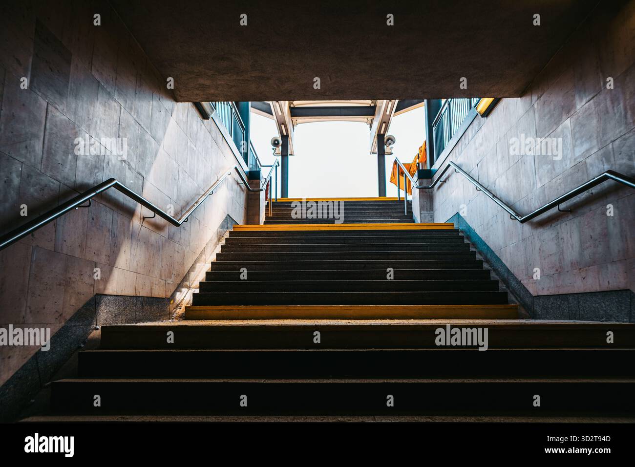 Vista dal fondo di una scala che porta al livello della strada in una metropolitana urbana o sottopassaggio. La luce del sole illumina l'uscita incorniciata da pareti in cemento, m Foto Stock