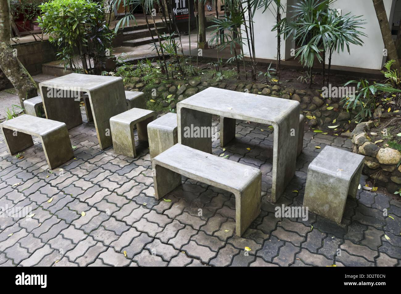 Tranquillo tavolo in pietra e panca per sedersi all'aperto nel patio del giardino. Arredi minimalisti e contemporanei in cemento su pavimentazione grigia per Foto Stock