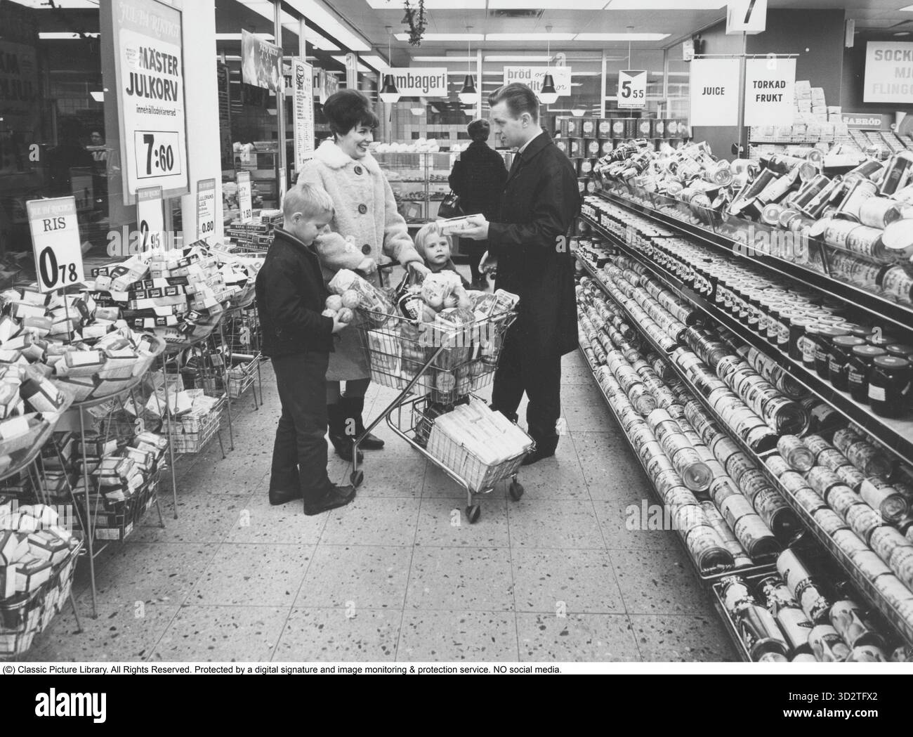 Shopping 1964. Interno di un negozio Co-op dove una famiglia con bambini sta facendo un grande negozio. Gli scaffali sono carichi di scatole e altri pacchetti, e la segnaletica evidenzia i prezzi allettanti del negozio. La moglie indossa un cappotto adatto al periodo e un elegante cappotto, mentre l'uomo sfoggia un trenchcoat elegante. Sia l'idea di self service che il carrello della spesa provenivano dall'America e miravano a ridurre le vendite. Il cliente poteva scegliere la spesa, mettere il carrello della spesa e procedere alla cassa del negozio. Foto Stock