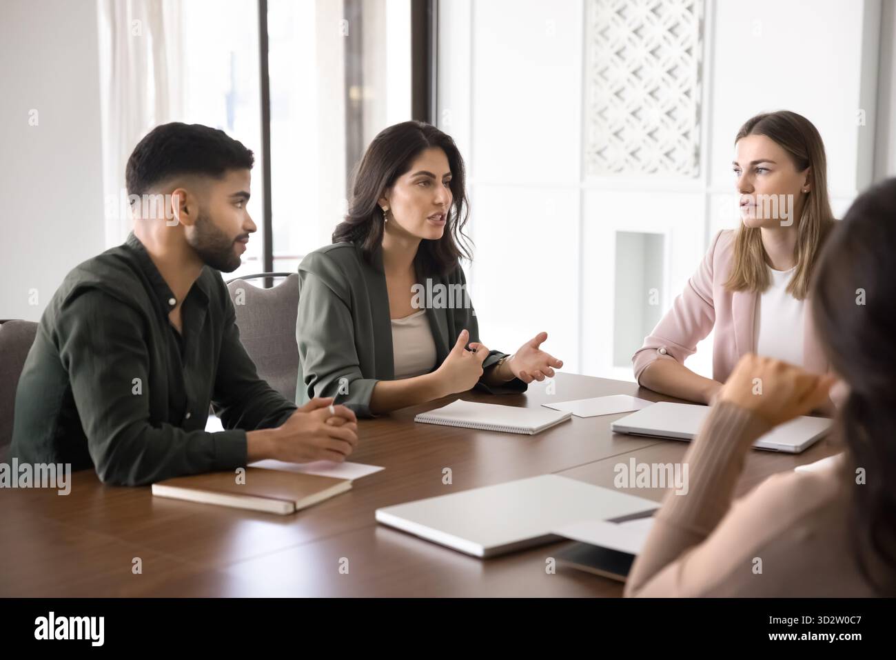 Il team di lavoro ascolta il collega alla scrivania per conferenze in un ufficio moderno Foto Stock