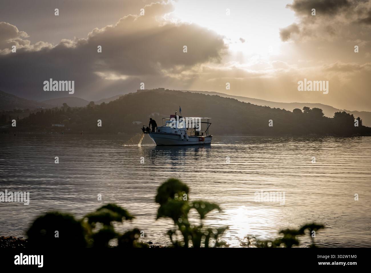 Il sole autunnale si infrangeva tra le nuvole e getta i raggi del sole sul mare naturale con una piccola barca da pesca e un pescatore che controllava il loro pescato. Foto Stock