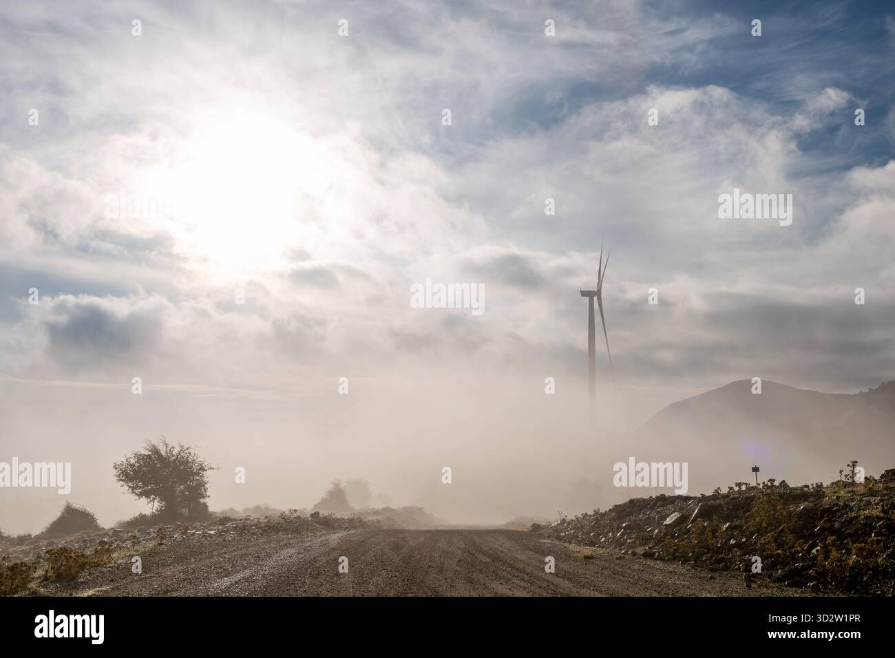 Una turbina eolica su un parco eolico in cima a una montagna all'alba parzialmente ricoperta di nebbia. Foto Stock