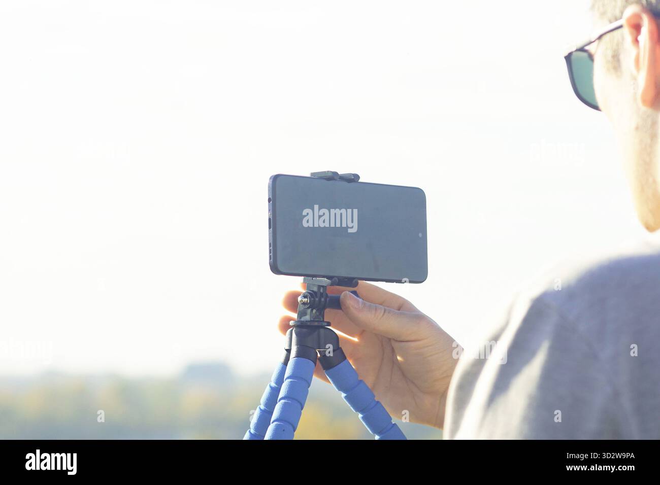 Mano che regge uno smartphone montato su un cavalletto flessibile all'aperto. Rappresenta uno strumento portatile per la creazione di contenuti e una soluzione di videografia economica. Foto Stock