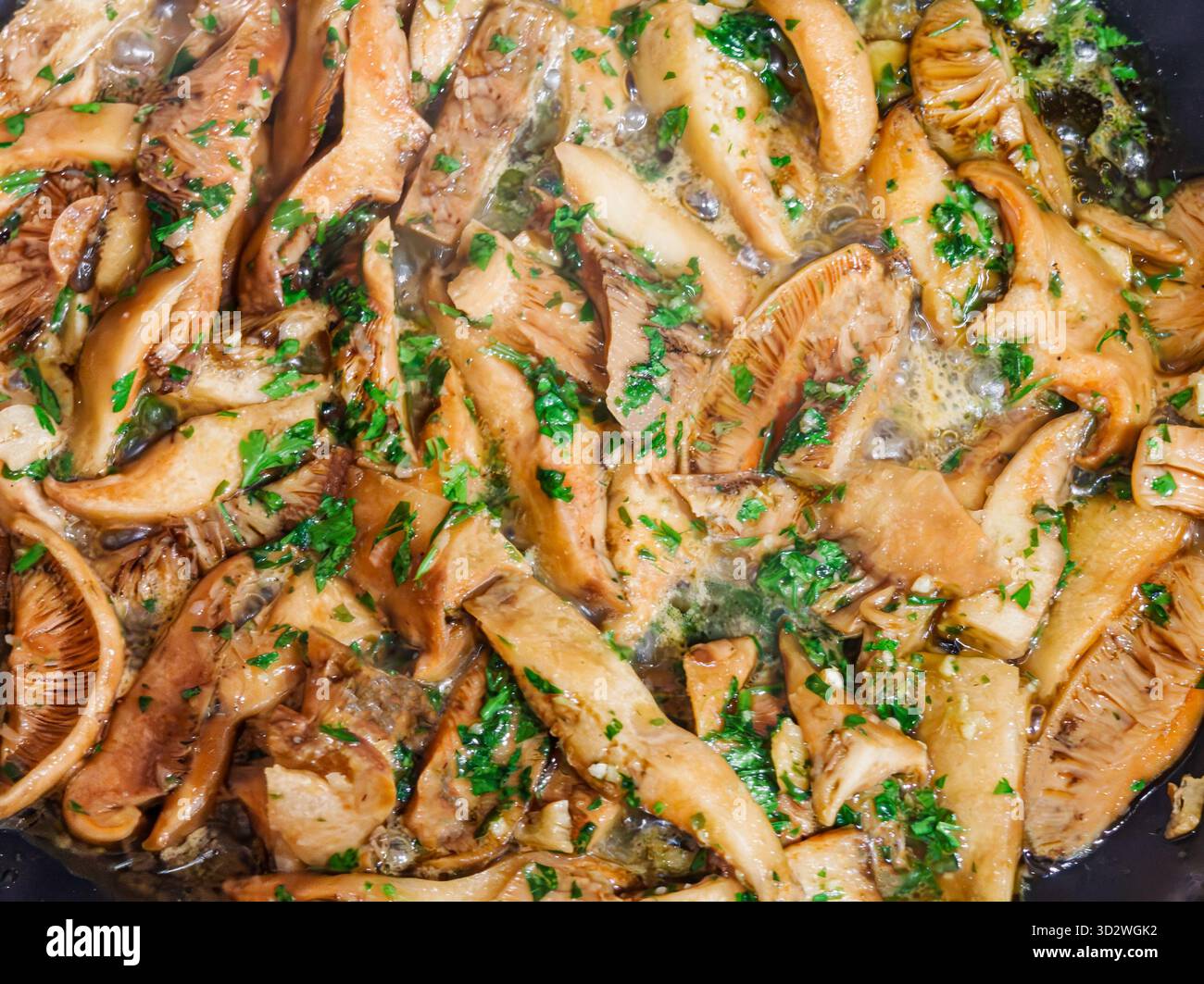 Primo piano di funghi selvatici cotti con aglio, prezzemolo e olio d'oliva in una padella. Piatto vegetariano mediterraneo tradizionale con consistenza dorata e fres Foto Stock