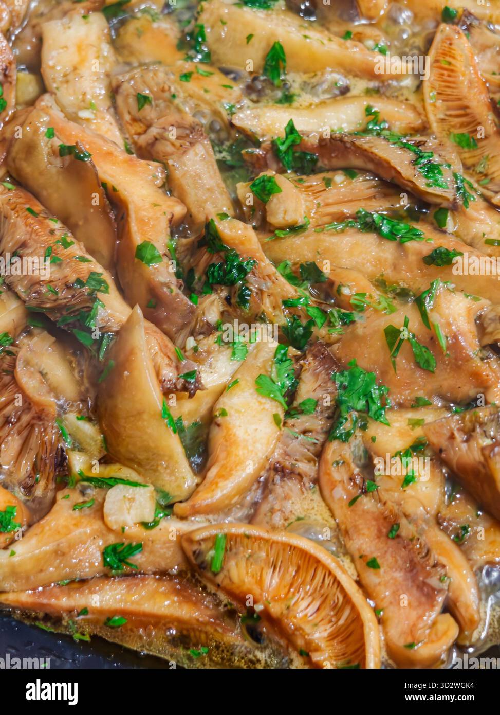 Primo piano di funghi selvatici cotti con aglio, prezzemolo e olio d'oliva in una padella. Piatto vegetariano mediterraneo tradizionale con consistenza dorata e fres Foto Stock