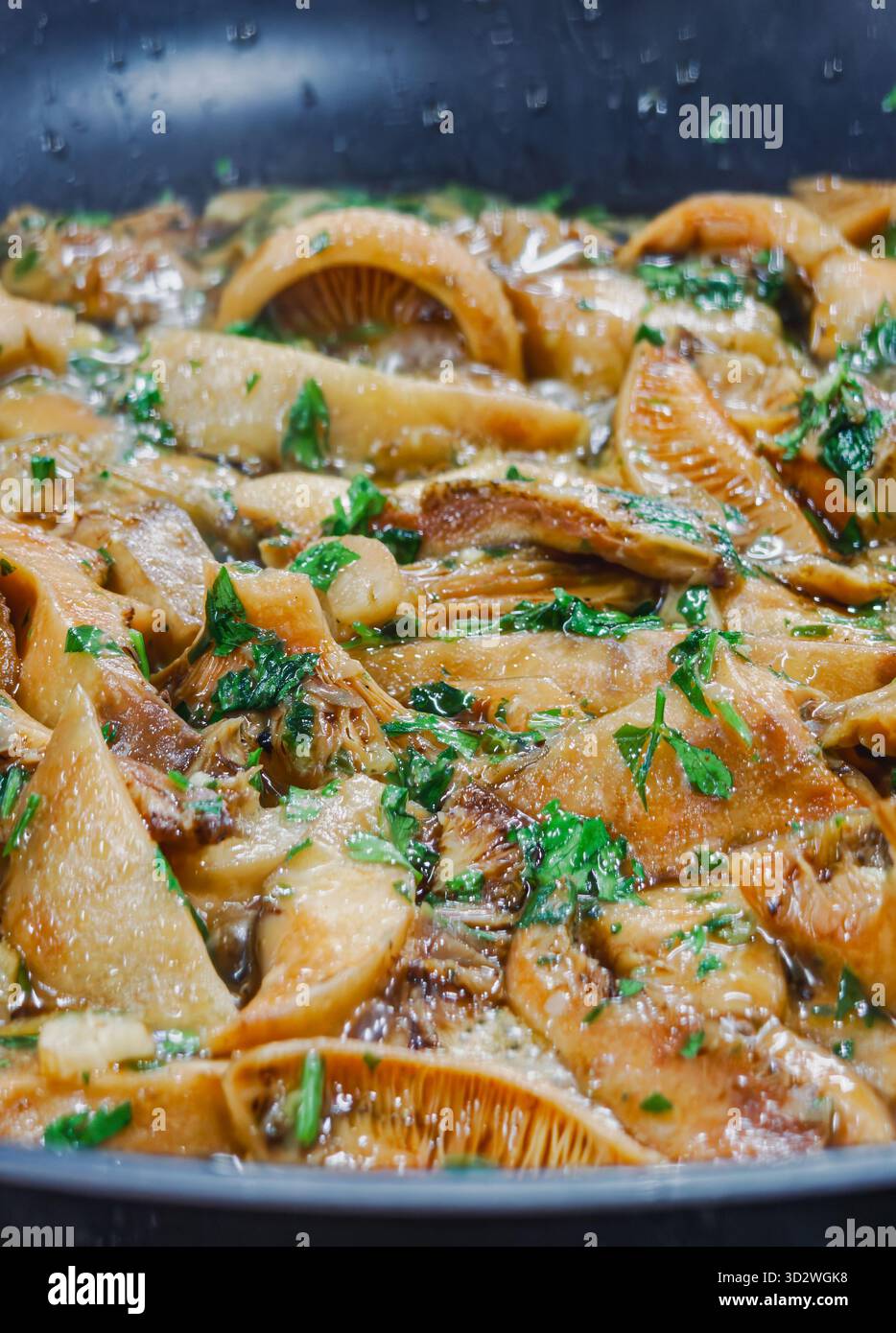 Primo piano di funghi selvatici cotti con aglio, prezzemolo e olio d'oliva in una padella. Piatto vegetariano mediterraneo tradizionale con consistenza dorata e fres Foto Stock