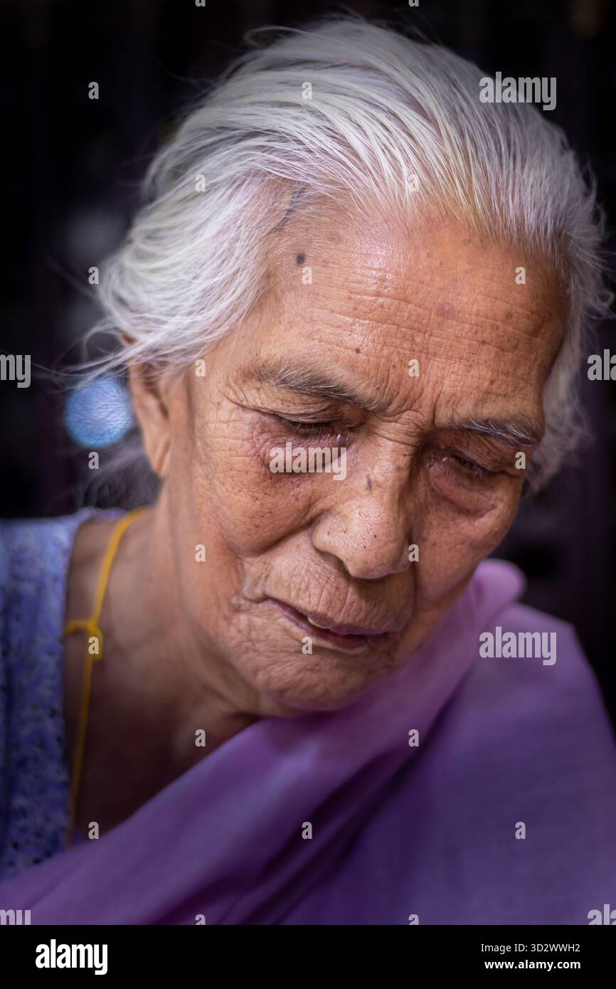Ritratto di una donna anziana al Tempio d'oro di Lalitpur saggezza e serenità nella valle di Kathmandu con il volto rivolto verso il basso Foto Stock