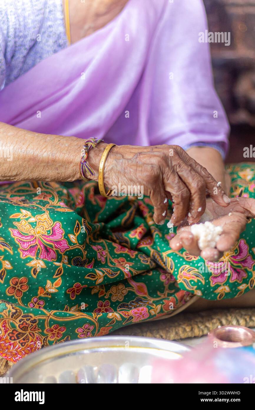 Le mani di una donna anziana preparano offerte al Tempio d'Oro di Lalitpur Uno sguardo di devozione e cultura Foto Stock