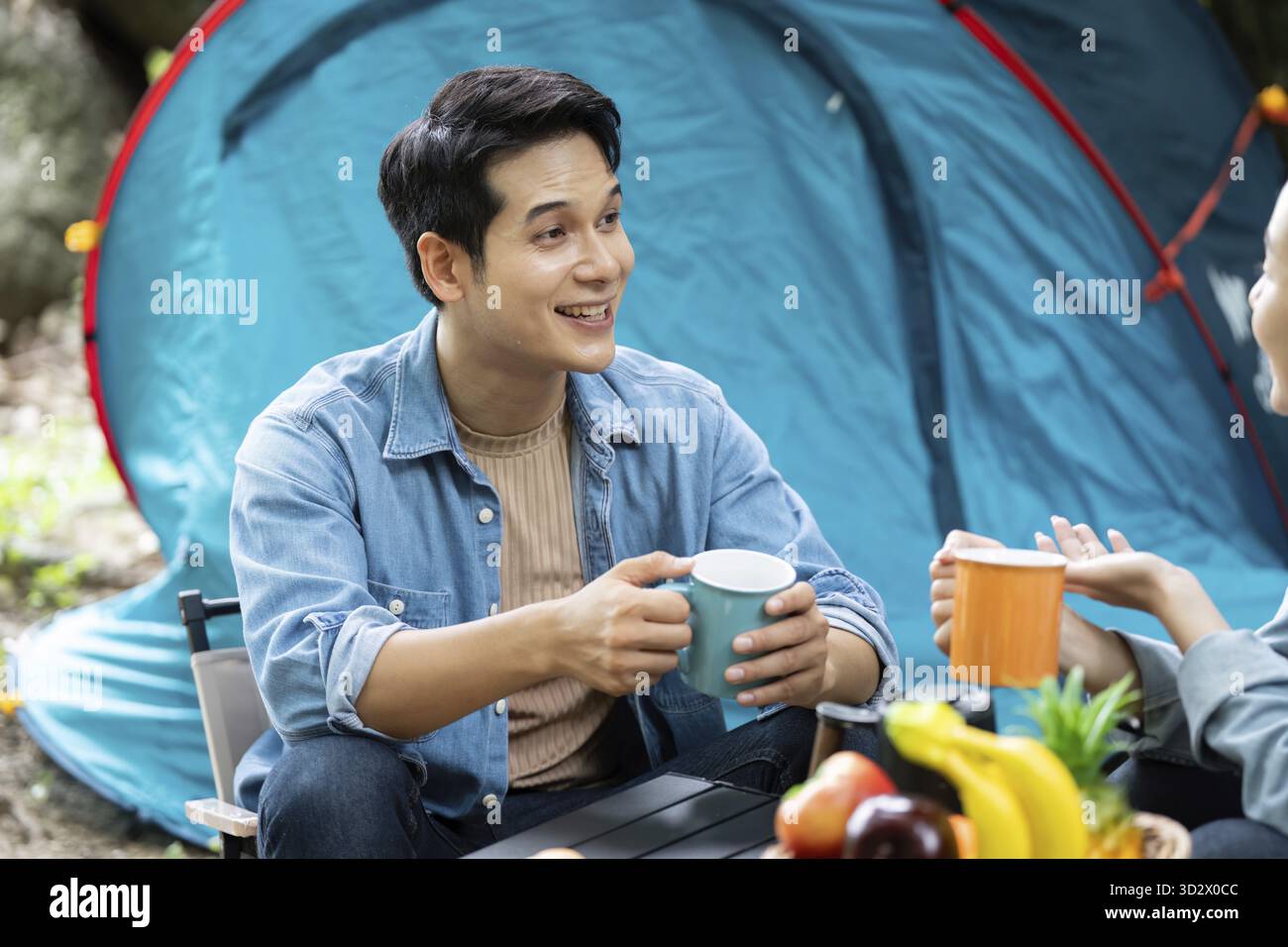 Una coppia felice che condivide caffè e risate in un campeggio, circondato dalla natura. Un momento perfetto di connessione e avventura all'aria aperta Foto Stock