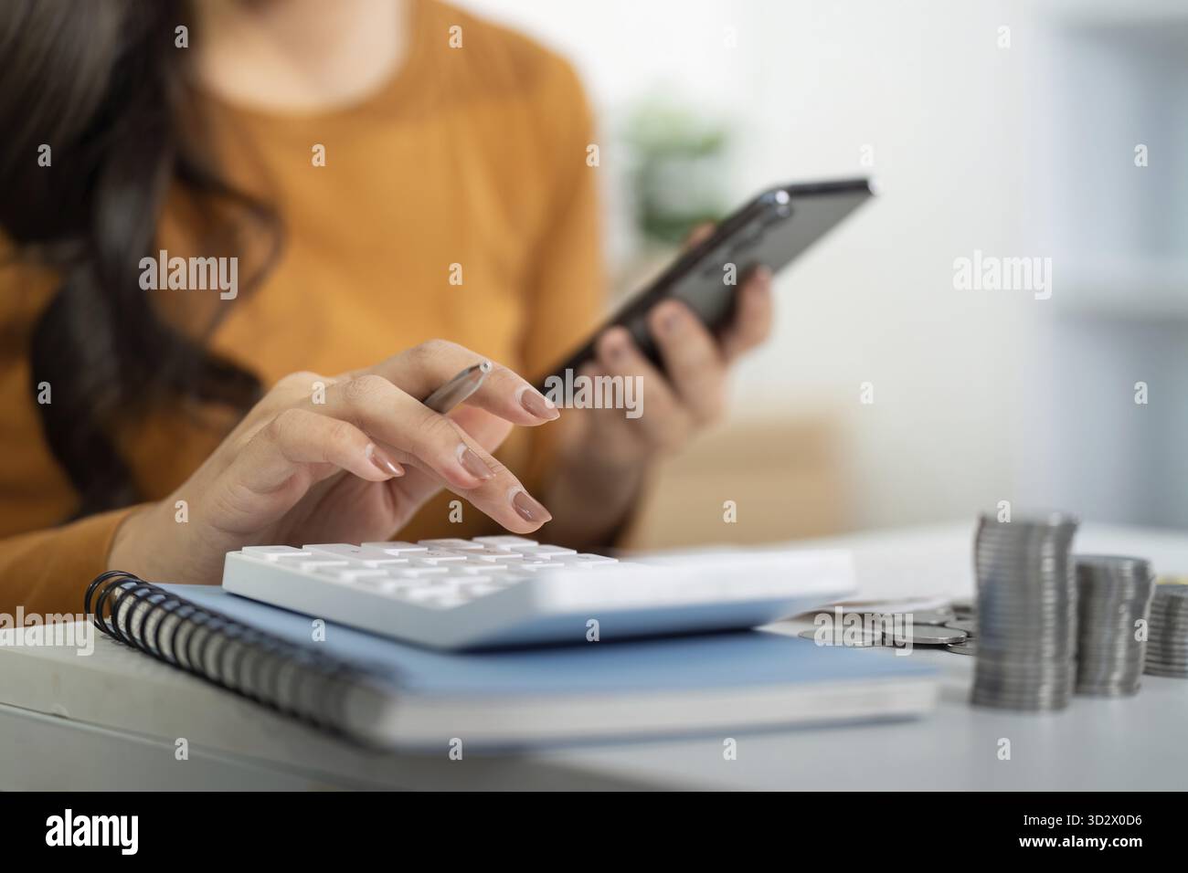 Una giovane donna impegnata nella pianificazione finanziaria, che utilizza una calcolatrice e uno smartphone per gestire il budget e le spese Foto Stock