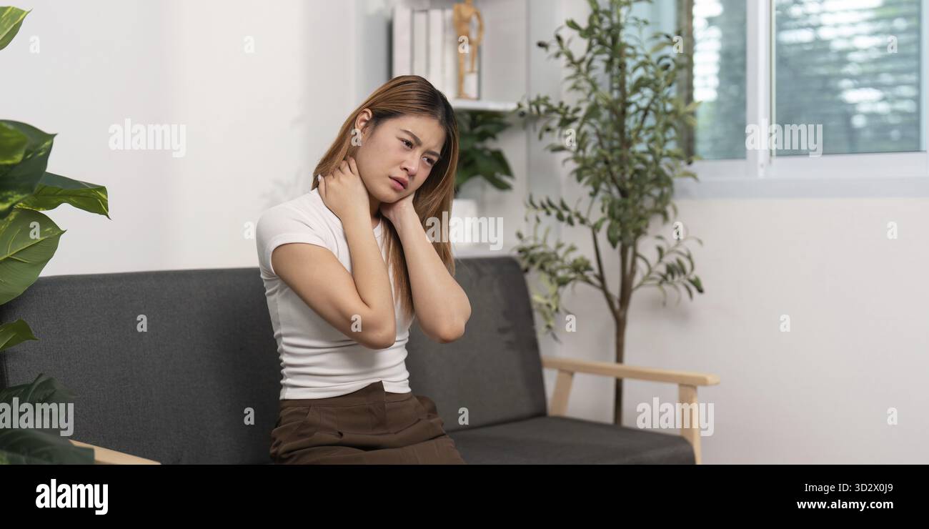 Una donna su un divano, che le tiene il collo nel dolore. Rappresenta la consapevolezza del dolore al collo e dei suoi effetti Foto Stock