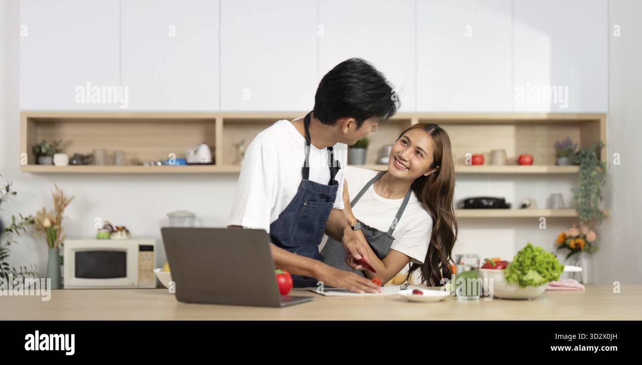 Una giovane coppia condivide un momento di gioco in cucina, preparando un pasto insieme e divertendosi come partner Foto Stock