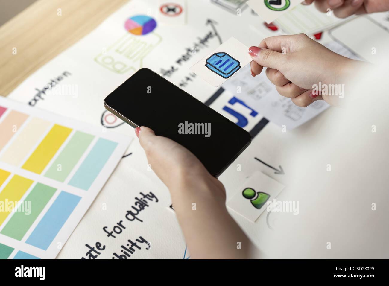Processo creativo nella progettazione di UX e UI con le mani che tengono lo smartphone e gli elementi di design su un tavolo. Concentrarsi sull'esperienza utente e sull'interfaccia Foto Stock