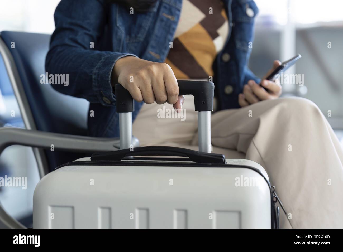 Un viaggiatore all'aeroporto prende i bagagli mentre utilizza il suo smartphone, segnalando la sua attesa per il viaggio che ci aspetta Foto Stock