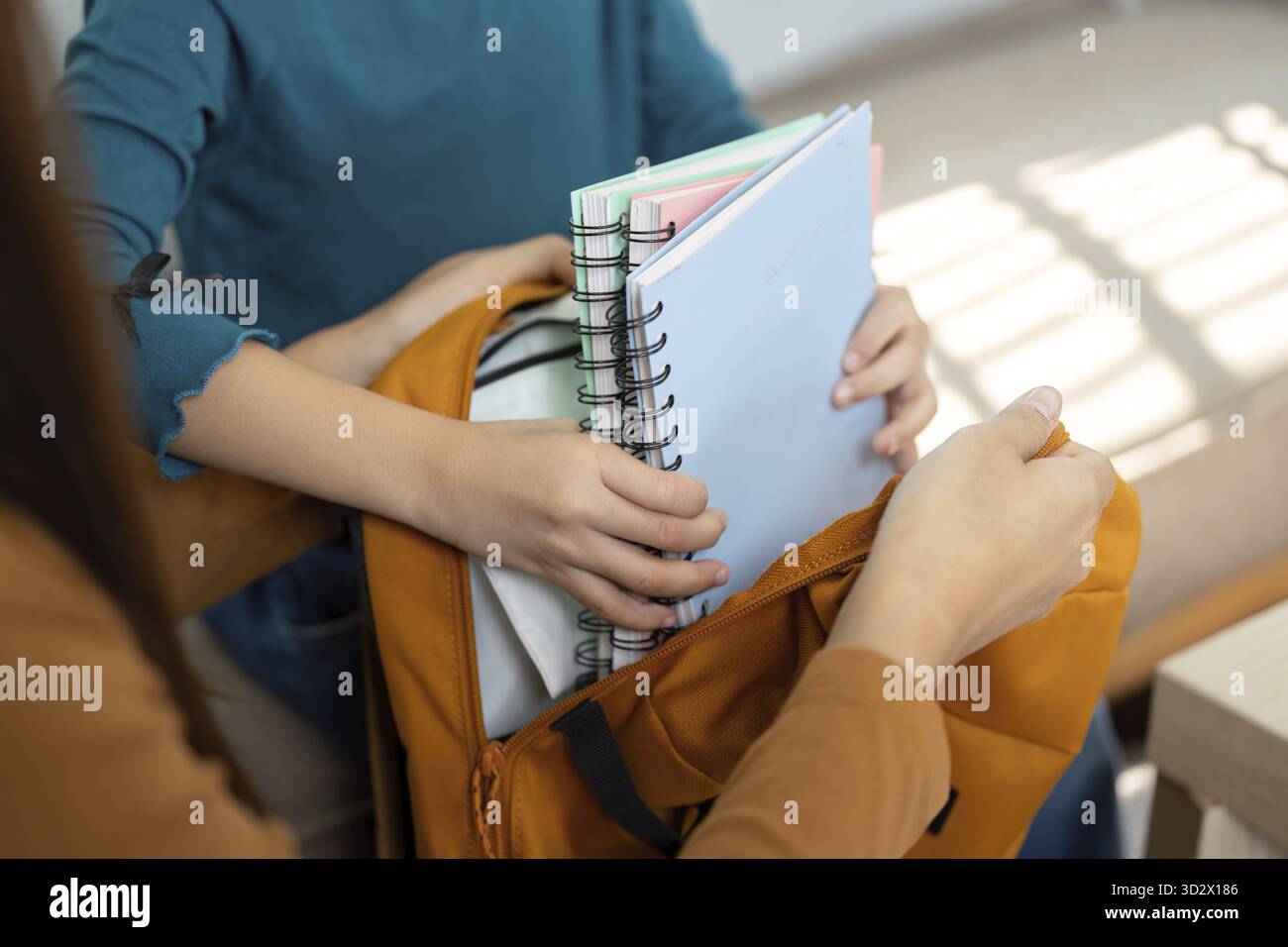 Una madre assiste sua figlia nel confezionare le forniture scolastiche essenziali in uno zaino arancione brillante, sottolineando l'importanza dell'organizzazione e della preparazione Foto Stock