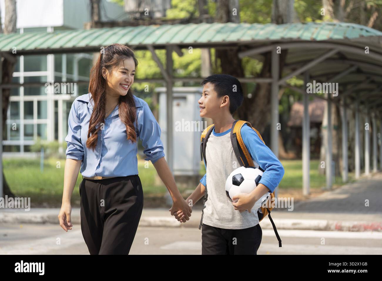 Questa scena toccante cattura una madre e un figlio che parlano animatamente mentre camminano verso la scuola, con sogni di calcio nell'aria Foto Stock