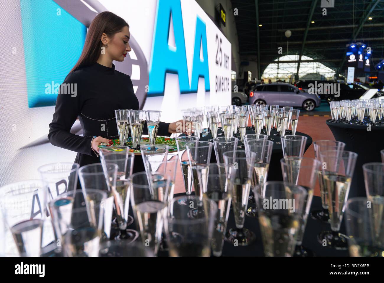 MINSK, BIELORUSSIA - 3 GIUGNO 2025: Una donna lavora in uno stand, che serve bevande al salone dell'auto Motorshow 2025. Un'auto rosa e uno schermo con testo in cirillico ar Foto Stock