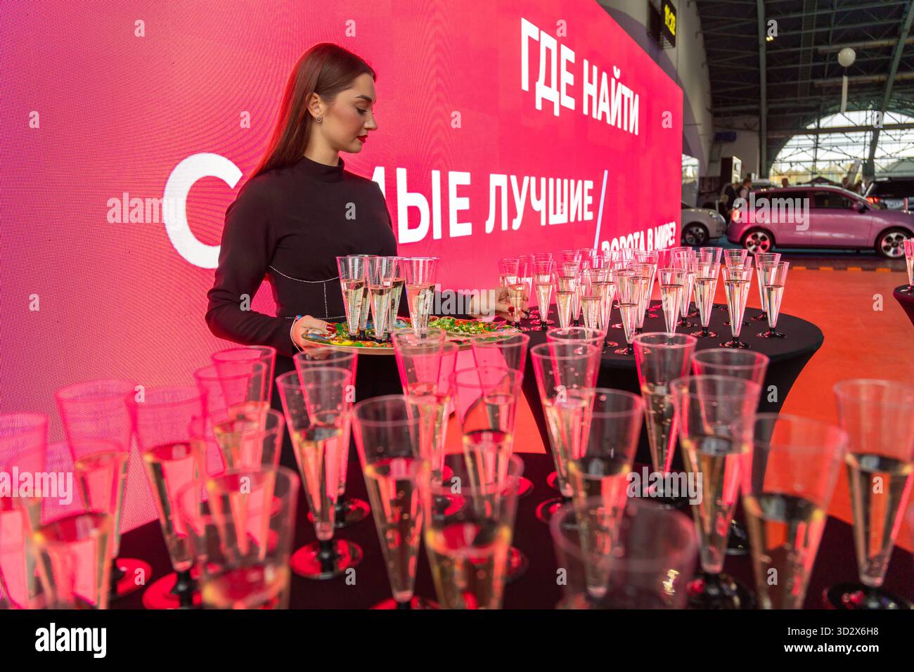 MINSK, BIELORUSSIA - 3 GIUGNO 2025: Una donna lavora in uno stand, che serve bevande al salone dell'auto Motorshow 2025. Un'auto rosa e uno schermo con testo in cirillico ar Foto Stock