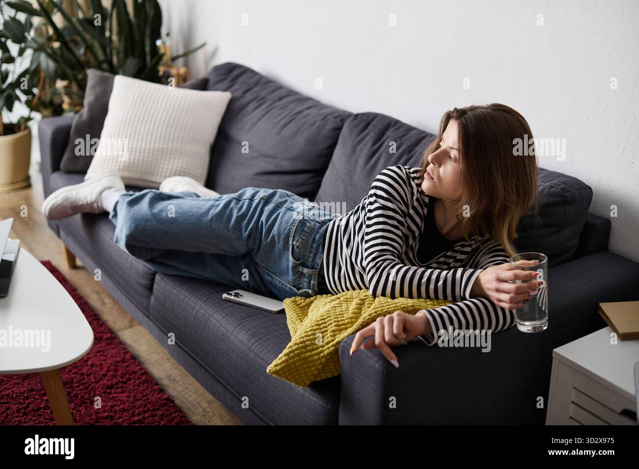 Una giovane donna si rilassa nel suo elegante appartamento, abbracciando una giornata con un drink in mano. Foto Stock