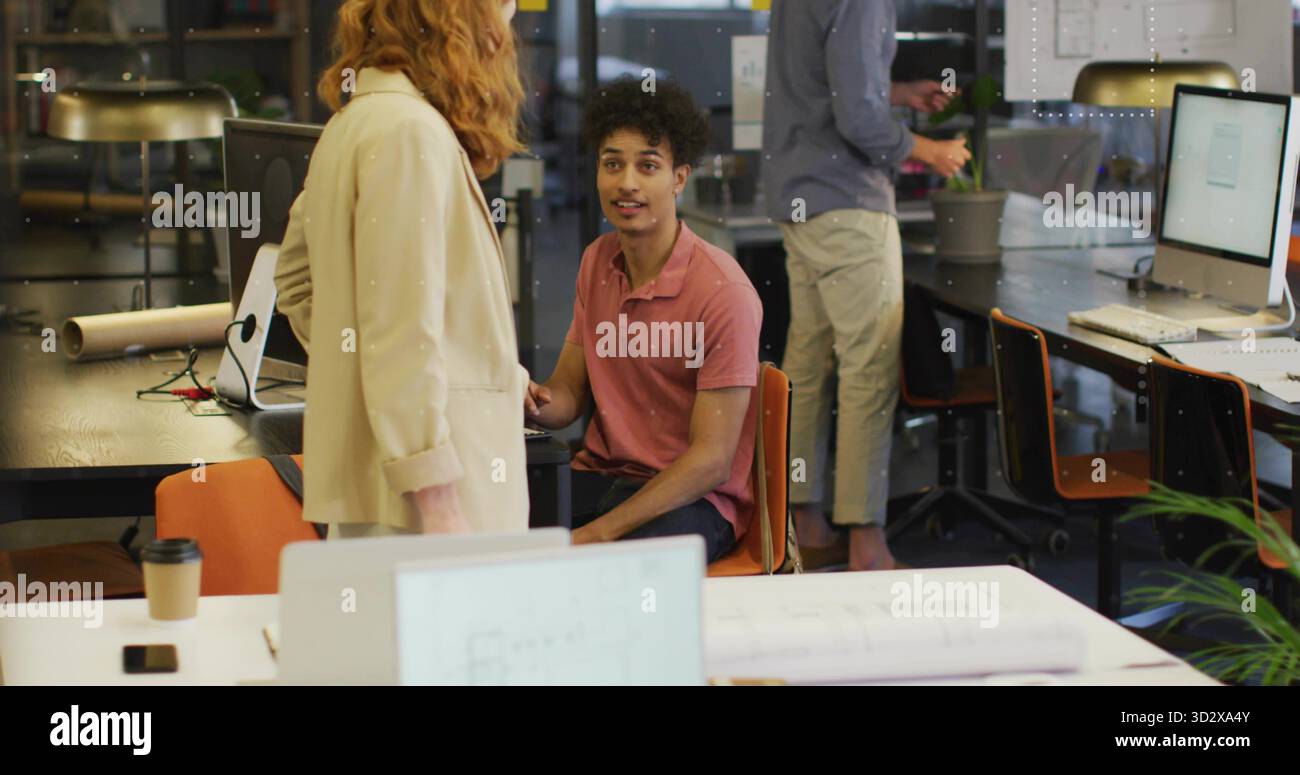Uomo ispanico e collega donna che rivede i progetti in un ufficio open space, con laptop e monitor Foto Stock
