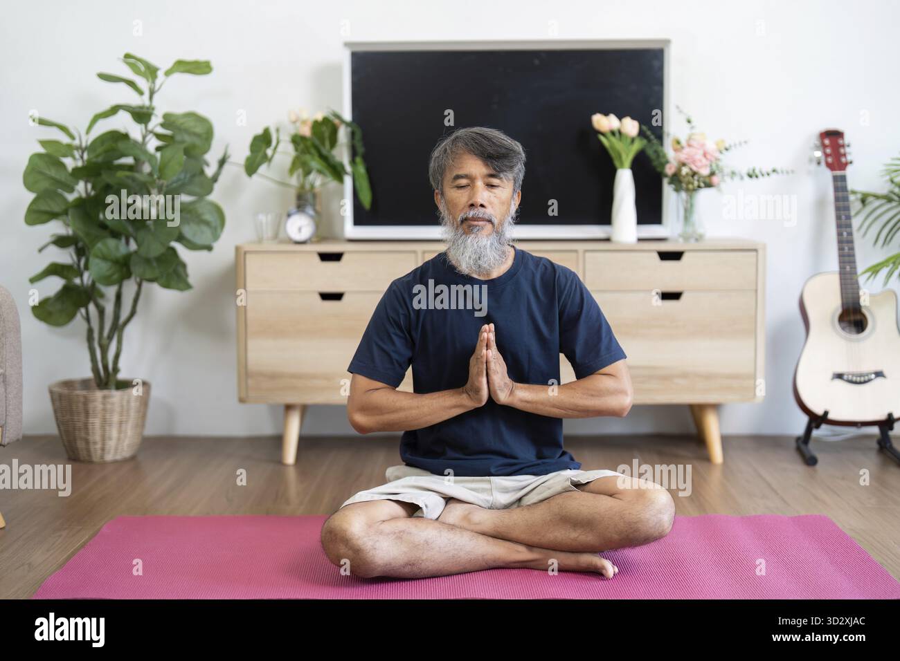 Un uomo anziano si siede in una rilassante posa yoga a casa, concentrandosi sul benessere mentre pratica tecniche di consapevolezza e rilassamento Foto Stock