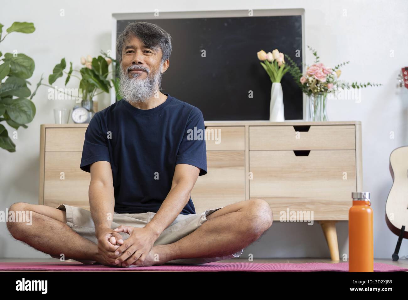 Un uomo anziano che medita con calma in un ambiente sereno a casa, migliorando il suo benessere e la sua consapevolezza attraverso tecniche di rilassamento Foto Stock